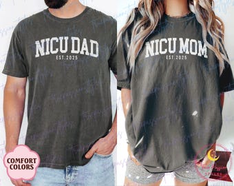 May include: Two dark gray t-shirts. One says "NICU DAD EST. 2025" in white block letters. The other says "NICU MOM EST. 2025" in white block letters. Both shirts have a vintage, distressed look.