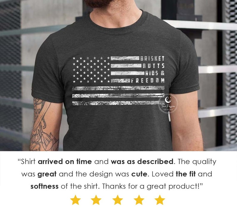 May include: A dark grey t-shirt with a distressed white American flag design. The text "BRISKET BUTTS RIBS & FREEDOM" is printed on the flag.