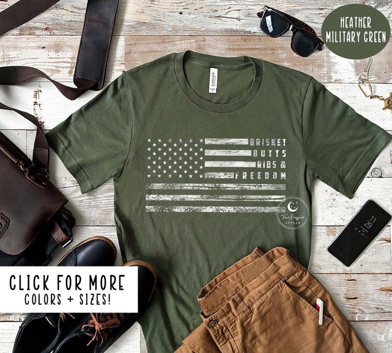 May include: A green t-shirt with a distressed white American flag design and the text "BRISKET RUTTS RIBS & FREEDOM". The shirt is available in multiple colors and sizes.