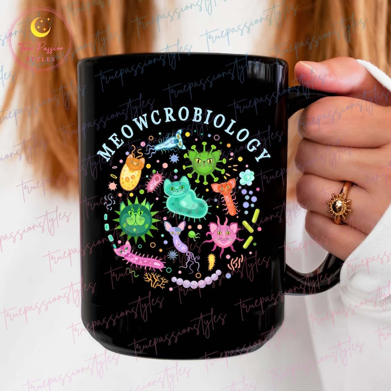 Puede incluir: Taza de caf&eacute; negra con un dise&ntilde;o circular blanco con el texto "MEOWCROBIOLOGY" y gatos y microbios de dibujos animados de colores.