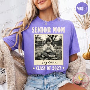 Może przedstawiać: Fioletowa koszulka z napisem "SENIOR MOM" pogrubioną czcionką. Poniżej czarno-białe zdjęcie dziecka. Imię "Taylor" jest napisane pod zdjęciem, z "CLASS OF 2027" i gwiazdkami.