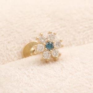 Può includere: Un orecchino a lobo in oro con un design a forma di fiore, caratterizzato da sei pietre bianche trasparenti a taglio rotondo che circondano una singola pietra centrale blu a taglio rotondo. Il gioiello presenta una chiusura piatta.