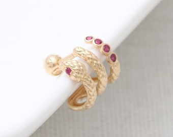 May include: Gold snake ear cuff with pink gemstones. The cuff is made of three intertwined snake bodies.