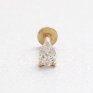 Pode incluir: Um brinco individual dourado com uma gema clara em forma de pêra. O brinco tem uma parte traseira plana e redonda e um pino para perfurar. A gema é facetada, captando a luz e adicionando brilho.