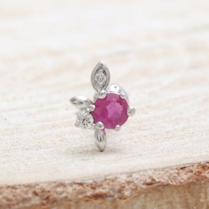 Może przedstawiać: Delikatny srebrny kolczyk z różowym rubinem otoczonym mniejszymi białymi diamentami. Kolczyk ma kwiatowy wzór z liściastymi akcentami.