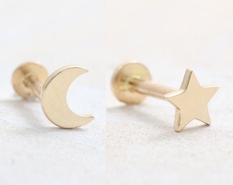May include: Two gold-coloured earrings. One earring features a crescent moon design, and the other has a star shape. Both earrings have a post and backing. The earrings are set against a white background.