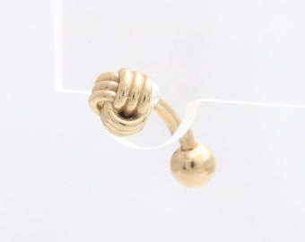 Op de afbeelding: Een gouden oorbel in de vorm van een knoop met een bol aan het uiteinde van de pen.