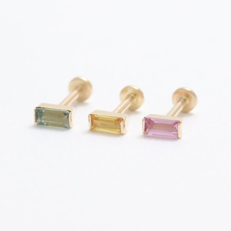 May include: Three gold stud earrings, each with a rectangular gemstone. The gemstones are green, yellow, and pink. The earrings are presented against a white backdrop. The gemstones are approximately 5mm in length.