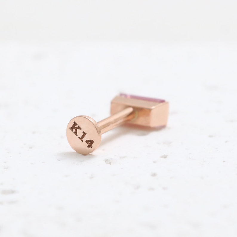 May include: A rose gold earring with a rectangular pink gemstone. The earring post has a circular backing stamped with "K14". The jewellery is set against a white background.
