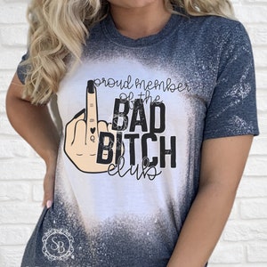 Puede incluir: Una camiseta blanca con un dise&ntilde;o salpicado de lej&iacute;a. La camiseta presenta una ilustraci&oacute;n en blanco y negro de un dedo medio con un coraz&oacute;n y las palabras "Proud member of the Bad Bitch Club".