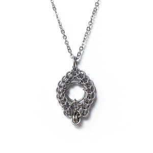 May include: A silver chain necklace with a circular pendant made of interwoven metal rings. The pendant has a smaller circle in the center.