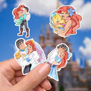 May include: Four die-cut stickers featuring cartoon characters with red hair, a prince in a white uniform, and a yellow fish. The illustrations depict romantic scenes and a hug, rendered in vibrant colors with white borders on a clear backing.