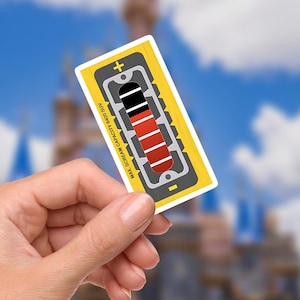 May include: A rectangular sticker with a yellow border and a battery-like graphic. The graphic shows a series of red and black bars, indicating a level. The text "MAX. SCREAM CAPACITY 8400 SUV" is printed on the left side. The background is a blurred image of a blue sky and a castle.