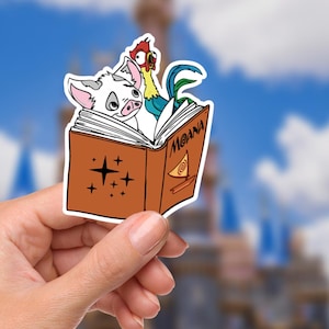 May include: A colorful sticker featuring characters from the animated film "Moana." The sticker shows a pig and a rooster peeking out from a book with the title "Moana." The book is brown with star and swirl designs.