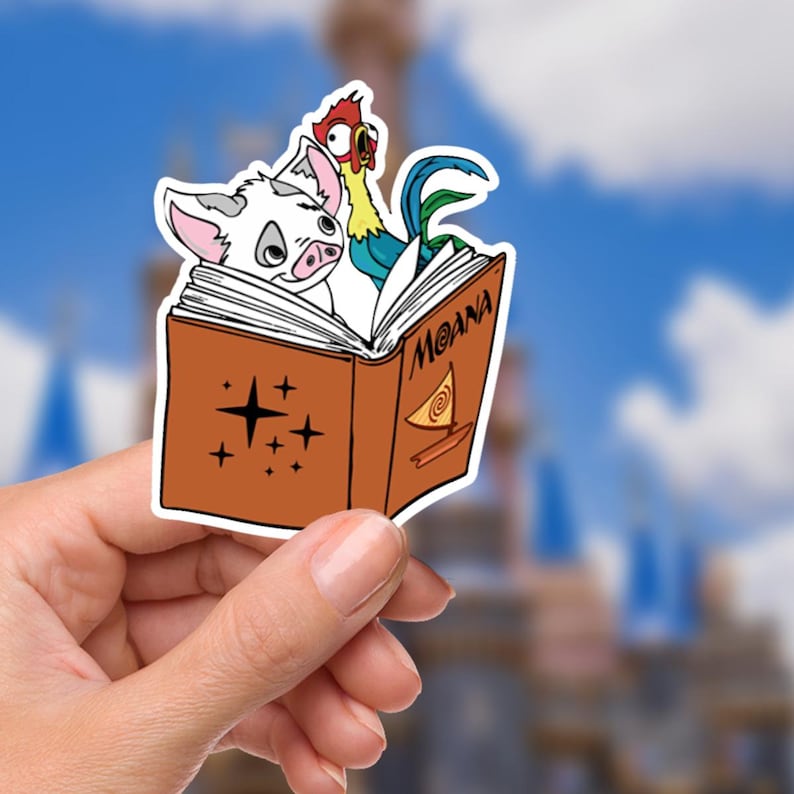 May include: A colorful sticker featuring characters from the animated film "Moana." The sticker shows a pig and a rooster peeking out from a book with the title "Moana." The book is brown with star and swirl designs.