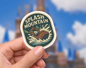 May include: A sticker featuring the words "SPLASH MOUNTAIN" in a vintage style. The design includes a log flume ride with water splashing, set against a backdrop of a mountain and a blue sky. The sticker is held by a hand.