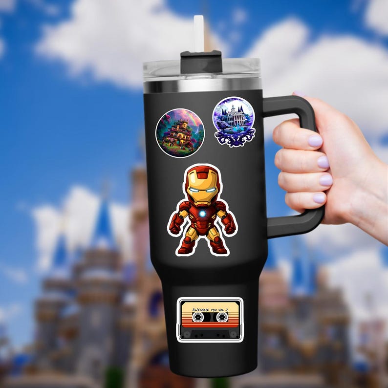 K&ouml;nnte beinhalten: Schwarzer isolierter Becher mit Griff, verziert mit Aufklebern von Iron Man, einem Spukhaus, einem Schloss und einer Retro-Kassette mit der Aufschrift "Awesome Mix Vol. 2". Der Becher hat einen transparenten Deckel und einen wei&szlig;en Strohhalm.