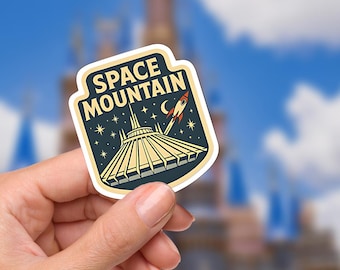 May include: A Space Mountain sticker featuring the ride's logo, a rocket, stars, and a crescent moon. The sticker has a navy blue background with beige and yellow accents. The words "Space Mountain" are printed at the top.