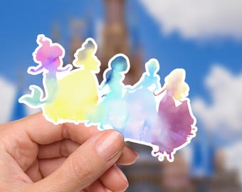 May include: A colorful sticker featuring watercolor silhouettes of five princesses. The sticker has a white border and a gradient of colors, including pink, yellow, blue, and purple. The background is a blurred image of a castle and a blue sky.