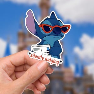 Può includere: Un adesivo di un personaggio blu dei cartoni animati con occhiali da sole rossi, che tiene in mano un giornale, con la scritta "silently judging" in rosso. Il personaggio è un popolare personaggio Disney.