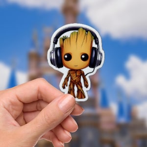 Puede incluir: Una pegatina con un personaje de dibujos animados con cuerpo de madera, ojos negros grandes y una pequeña sonrisa. El personaje lleva auriculares negros. El fondo es una imagen borrosa de un castillo y un cielo azul con nubes.