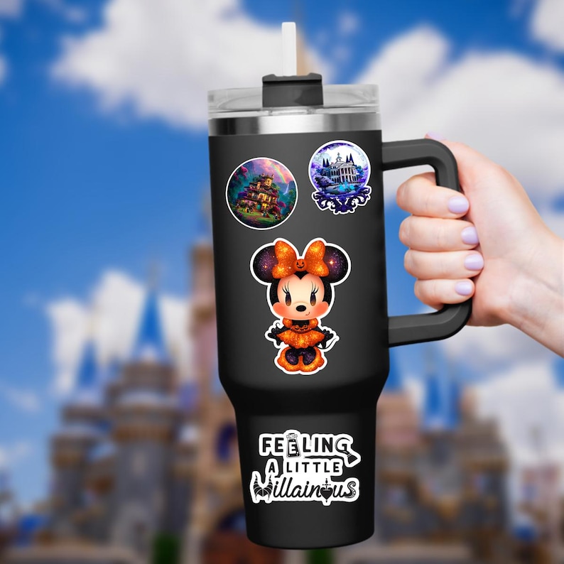 May include: Black tumbler with a handle and straw, decorated with Halloween-themed stickers. Stickers include a cartoon Minnie Mouse in a Halloween costume, a haunted house, and the text "Feeling a little villainous."