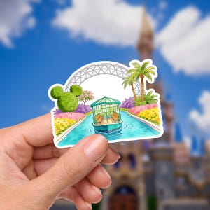 May include: A colorful sticker featuring a boat ride scene with a green gazebo-like structure, palm trees, and a Mickey Mouse-shaped topiary. The sticker has a blue sky background with a castle in the distance.