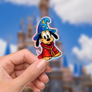 May include: A colorful sticker featuring a cartoon dog dressed as a wizard. The dog wears a blue hat with a crescent moon and a red robe. The sticker has a holographic finish and is held against a blurred background.