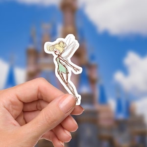 May include: A sticker of a cartoon fairy with blonde hair, a green dress, and wings. The fairy is in a flying pose. The background is a blurred image of a castle and a blue sky with clouds.