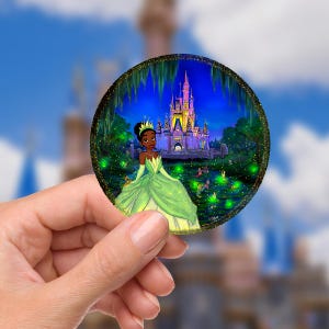 Pode incluir: Ilustração redonda com uma princesa em um vestido verde, com um castelo e uma cena noturna com luzes brilhantes. A princesa está usando uma coroa e joias.