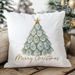 May include: White square pillow with a watercolor design of a Christmas tree made of blue and gold oyster shells, topped with a gold star. The words "Merry Christmas" are written in gold script below the tree.