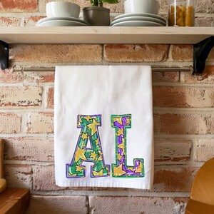 Könnte beinhalten: Weißes Küchentuch mit den Buchstaben "AL" in Grün, Lila und Gelb mit einem Sternmuster.