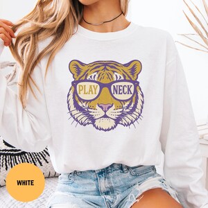 May include: White sweatshirt featuring a tiger face graphic wearing glasses with the words "PLAY NECK" in a purple and gold design. The tiger graphic is centered on the front of the long-sleeved top. The sweatshirt is made of a soft material.