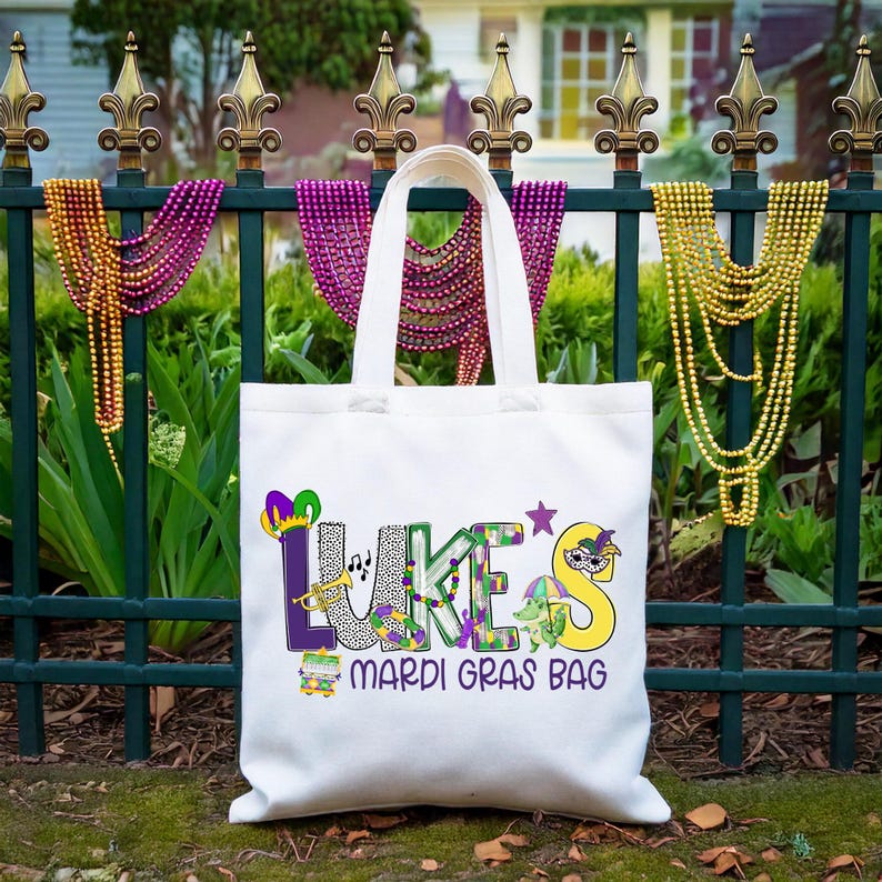 May include: White canvas tote bag with the name "Lukes" in colorful letters and Mardi Gras themed decorations. The text "Mardi Gras Bag" is printed below the name.