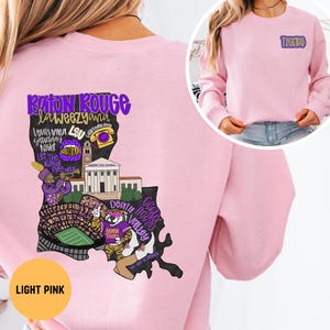 May include: Light pink sweatshirt with a graphic of the Louisiana state map, featuring text like "Baton Rouge" and "Death Valley." The word "Tigers" is on the upper right. The bottom left corner has the text "Light Pink."