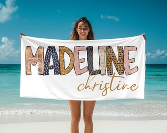 May include: A white beach towel with the name "Madeline christine" written in colorful patterned letters. The letters are in shades of pink, blue, yellow, and brown.