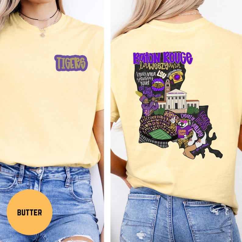 May include: A light yellow t-shirt with the word "TIGERS" in purple on the front. The back of the shirt features a purple and gold graphic of Louisiana with text that says "Baton Rouge, Laweeziana, Louisiana LSU Saturday Night".