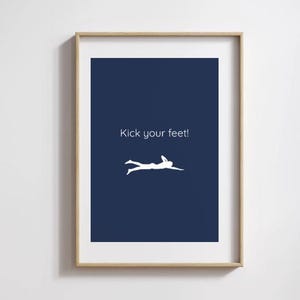 May include: Framed art print featuring a navy blue background with the text "Kick your feet!" in white. A white silhouette of a person swimming is below the text. The frame is a light wood color.