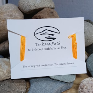 Puede incluir: Una tarjeta blanca con un logotipo negro de una monta&ntilde;a y un r&iacute;o con el texto "Tenkara Path" y "12' (365cm) braided level line". La tarjeta tiene una l&iacute;nea trenzada amarilla adjunta.