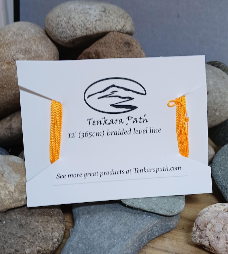 Puede incluir: Una tarjeta blanca con un logotipo negro de una monta&ntilde;a y un r&iacute;o con el texto "Tenkara Path" y "12' (365cm) braided level line". La tarjeta tiene una l&iacute;nea trenzada amarilla adjunta.