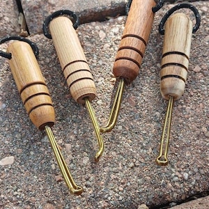 May include: Four wooden latch hook tools with brass hooks and black loops at the top. The wooden handles have a series of black rings. The tools are arranged on a textured stone surface.
