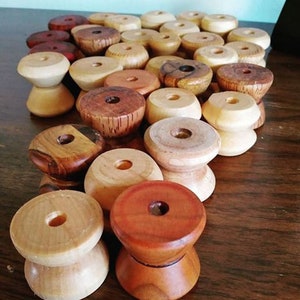 Puede incluir: Una colección de carretes de madera en varios tonos de marrón, rojo y madera natural. Los carretes tienen un agujero en el centro y están apilados en forma de pirámide.