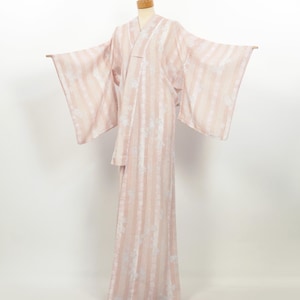 Puede incluir: Una bata estilo kimono a rayas rosas y blancas con detalles florales. La bata tiene mangas anchas y un diseño envolvente. La tela parece ligera y fluida, adecuada para descansar o como cubierta.