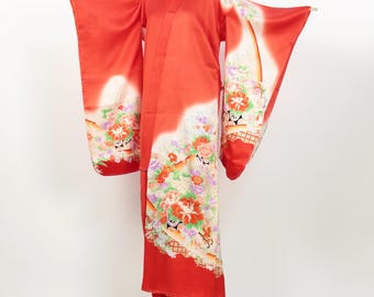May include: A bright red kimono with floral patterns and white detailing. The traditional Japanese garment is displayed on a mannequin, showcasing its long sleeves and intricate design. The kimono features a V-neck and is made of a smooth, flowing fabric.