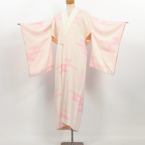 May include: A light pink kimono with a white collar and pink cloud-like patterns. The kimono is displayed on a mannequin with its arms extended, showcasing the full length and design. The fabric appears to have a subtle texture.