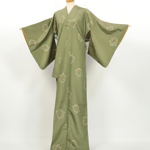 May include: A sage green kimono with a geometric pattern of squares and red accents. The kimono has wide sleeves and a wrap-around design. The sleeves have a gold trim. The garment is displayed on a mannequin.
