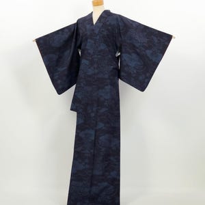 May include: A dark navy blue kimono featuring a tonal, repeating pattern of stylized clouds and floral motifs. The garment has wide, rectangular sleeves, a V-neckline, and a full-length silhouette, displayed on a neutral-toned mannequin.
