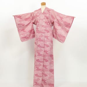 May include: A full-length kimono featuring a repeating pattern of white and dark pink fan-shaped motifs. The garment has wide, rectangular sleeves and a V-neckline, displayed on a mannequin to show the structure of the fabric and the design.