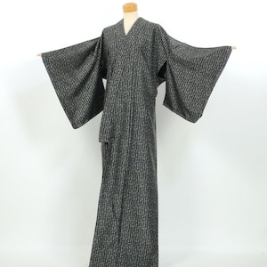 May include: A full-length kimono featuring a dark charcoal gray base color with a repeating vertical pattern of small, light-colored floral or geometric motifs. The garment has wide, extended sleeves and a traditional wrap-front neckline.
