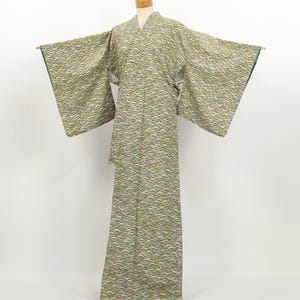 May include: A full-length kimono featuring a repeating pattern of stylized waves in shades of sage green, white, and muted gold. The garment has wide, rectangular sleeves, a V-neckline, and a straight-cut silhouette displayed on a mannequin.
